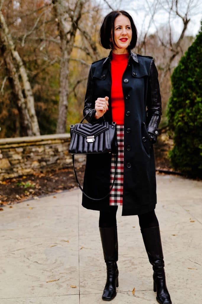 April from Stunning Style wearing a stylish winter outfit featuring a red top and plaid skirt with long black coat.