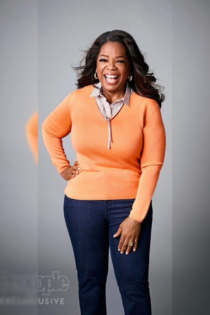 Oprah Winfrey wearing an orange top and jeans.